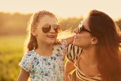 Happy fashion kid girl embracing her mother in trendy sunglasses and looking each other with love on nature background. Closeup royalty free stock photography Happy fashion kid girl embracing her mother in trendy sunglasses and looking each other with love on nature background. Closeup royalty free stock photography