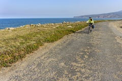 Happy female cyclist rides bicycle on road along ocean shore. Stock Photos Happy female cyclist rides bicycle on road along ocean shore. Stock Photos