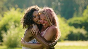 Happy female friends hugging and laughing at summer Color festival, slow motion