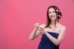 A happy girl, with hair curlers and in a bath towel, filings nails with a nail file and smiles. Pink background. stock photography A happy girl, with hair curlers and in a bath towel, filings nails with a nail file and smiles. Pink background. stock photography