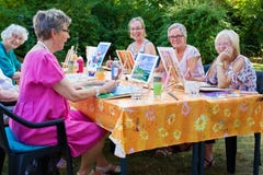 Happy group of senior ladies enjoying art class seated around a table outdoors in the garden painting with water colors while royalty free stock photos Happy group of senior ladies enjoying art class seated around a table outdoors in the garden painting with water colors while royalty free stock photos