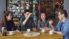 Happy handsome guy is telling funny story to his friends while dining in cafe while his mates are laughing and doing stock footage Happy handsome guy is telling funny story to his friends while dining in cafe while his mates are laughing and doing stock footage