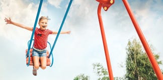 Happy little child girl laughing and swinging on a swing in the stock photo Happy little child girl laughing and swinging on a swing in the stock photo