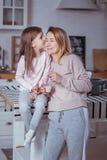 Happy little girl and her beautiful young mother have breakfast together in a white kitchen. Daughter kisses her mom. Maternal stock images Happy little girl and her beautiful young mother have breakfast together in a white kitchen. Daughter kisses her mom. Maternal stock images