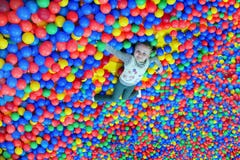 Happy little girl lays on the big heap of multicolored small balls