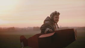 Happy little pilot boy starts to run in fun cardboard plane on sunset autumn field, playing and having fun slow motion.