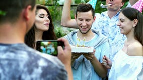 Happy man celebrates a birthday, blows out candles on a cake, friends congratulate, take a photo on mobile phone stock video Happy man celebrates a birthday, blows out candles on a cake, friends congratulate, take a photo on mobile phone stock video
