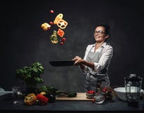 Happy Middle-aged Female Chef Tossing Chopped Vegetables In The Air From A Frying Pan Stock Photography Happy Middle-aged Female Chef Tossing Chopped Vegetables In The Air From A Frying Pan Stock Photography