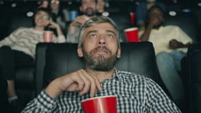 Happy middle-aged man is laughing eating popcorn watching movie in cinema stock video Happy middle-aged man is laughing eating popcorn watching movie in cinema stock video