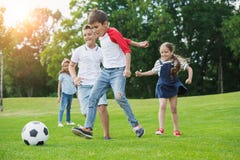 Happy multiethnic kids playing soccer with ball in park