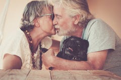 Happy Old Senior Couple People In Love Kiss Eachother And Hug Their Lovely Black Dog Pug - Home Leisure Activity And Forever Stock Image