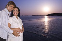 Happy pregnant couple on beach at sunrise