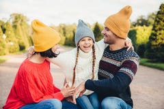 Happy small girl embrace her mother and father, have fun together, walk in beautiful park or on road. Parents look at her lovely d royalty free stock image Happy small girl embrace her mother and father, have fun together, walk in beautiful park or on road. Parents look at her lovely d royalty free stock image
