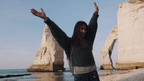Happy smiling brunette traveler woman with backpack spinning with arms open at rocky sea shore near Etretat slow motion. stock video footage Happy smiling brunette traveler woman with backpack spinning with arms open at rocky sea shore near Etretat slow motion. stock video footage