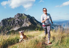 Happy smiling female jogging by the mounting range path with her beagle dog. Canicross running healthy lifestyle concept image