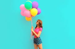 Happy smiling young woman with bunch of balloons looking up having fun wearing a shorts and pink t-shirt on blue wall