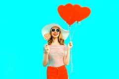 Happy smiling young woman with lollipop, red heart shaped air balloons in summer straw hat and shorts on colorful blue royalty free stock photography Happy smiling young woman with lollipop, red heart shaped air balloons in summer straw hat and shorts on colorful blue royalty free stock photography