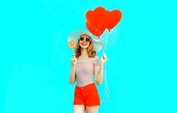 Happy smiling young woman with lollipop, red heart shaped air balloons in summer straw hat and shorts on colorful blue royalty free stock photo Happy smiling young woman with lollipop, red heart shaped air balloons in summer straw hat and shorts on colorful blue royalty free stock photo