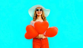 Happy smiling young woman with red heart shaped air balloons in summer straw hat and shorts on colorful blue royalty free stock photography Happy smiling young woman with red heart shaped air balloons in summer straw hat and shorts on colorful blue royalty free stock photography