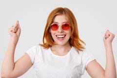 Happy successful ginger young female keeps clenched fists raised, has toothy smile, celebrates successful day, dressed in casual c stock image Happy successful ginger young female keeps clenched fists raised, has toothy smile, celebrates successful day, dressed in casual c stock image