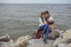 Happy thoughtful couple sitting on a rock beach near sea hugging stock photo Happy thoughtful couple sitting on a rock beach near sea hugging stock photo