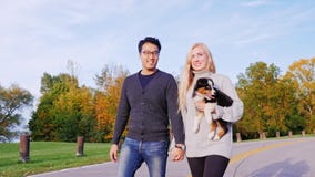 Happy Together With His Beloved Dog. Multiethnic Couple Walking In The Park With His Dog. Caucasian Woman Carries A Royalty Free Stock Photos