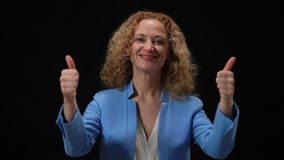 Happy woman showing thumbs up posing in camera flashes at black background. Portrait of smiling confident Caucasian