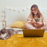 Happy woman sits with money on the bed and is educated online. Cat and girl while paying with dollars for work online