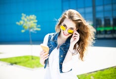 Happy young beautiful woman with curly hair and stylish sunglasses having fun and eating ice cream. Urban style. Outdoor shot. royalty free stock photography Happy young beautiful woman with curly hair and stylish sunglasses having fun and eating ice cream. Urban style. Outdoor shot. royalty free stock photography