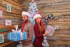 Happy couple in red elf hat, stand backs to each other and holding Christmas gift boxes. Indoors. stock image Happy couple in red elf hat, stand backs to each other and holding Christmas gift boxes. Indoors. stock image