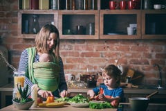 Happy young family, beautiful mother with two children, adorable preschool boy and baby in sling cooking together in a sunny kitch stock image Happy young family, beautiful mother with two children, adorable preschool boy and baby in sling cooking together in a sunny kitch stock image