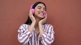 Happy young Latin woman having fun listening music with wireless headphones