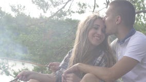 Happy young teenager couple fried sausages on smoky bonfire in the forest. Close-up stock video Happy young teenager couple fried sausages on smoky bonfire in the forest. Close-up stock video