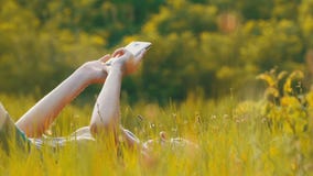 Happy Young Woman Lying on Green Lawn Uses Smartphone on Scenic Field at Sunset Background stock footage Happy Young Woman Lying on Green Lawn Uses Smartphone on Scenic Field at Sunset Background stock footage