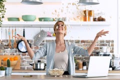 Happy Young Woman Tossing Popcorn Into The Air While Working On The Laptop At Home Royalty Free Stock Photos