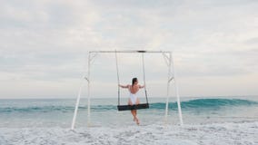 Happy young woman in white swimsuit riding on swing enjoying sea view. Vacation concept stock video footage Happy young woman in white swimsuit riding on swing enjoying sea view. Vacation concept stock video footage