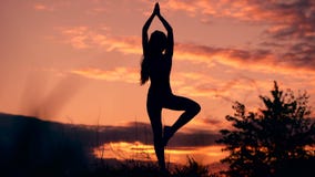 In harmony with oneself and the world. Silhouette of woman standing at yoga pose during an amazing sunset.