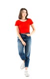 Hellång stående av en härlig ung flicka som bär den röda t-skjortan och jeans som lutar på en vägg på vit bakgrund, studiofors arkivfoto Hellång stående av en härlig ung flicka som bär den röda t-skjortan och jeans som lutar på en vägg på vit bakgrund, studiofors arkivfoto