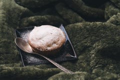 Hemlagad muffin med pudrat socker på en svart platta och en tesked på en bakgrund av gröna textiler arkivbilder Hemlagad muffin med pudrat socker på en svart platta och en tesked på en bakgrund av gröna textiler arkivbilder