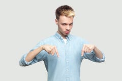 Here and right now. Portrait of serious handsome young man in light blue shirt standing, pointing his finger down, looking at stock images Here and right now. Portrait of serious handsome young man in light blue shirt standing, pointing his finger down, looking at stock images