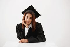 Het aantrekkelijke Afrikaanse vrouwelijke gediplomeerde glimlachen die camerazitting bekijken over witte achtergrond Royalty-vrije Stock Fotografie Het aantrekkelijke Afrikaanse vrouwelijke gediplomeerde glimlachen die camerazitting bekijken over witte achtergrond Royalty-vrije Stock Fotografie