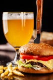 Het concept Italiaanse keuken Italiaanse hamburger met frieten op een houten raad en een glas licht bier met schuim stock afbeeldingen Het concept Italiaanse keuken Italiaanse hamburger met frieten op een houten raad en een glas licht bier met schuim stock afbeeldingen