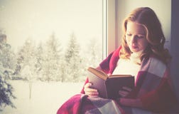 Het gelukkige boek van de meisjeslezing door het venster in de winter royalty-vrije stock afbeeldingen Het gelukkige boek van de meisjeslezing door het venster in de winter royalty-vrije stock afbeeldingen