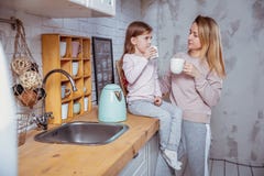 Het gelukkige meisje en haar mooie jonge moeder hebben samen ontbijt in een witte keuken Zij gieten en drinken thee moeder royalty-vrije stock foto Het gelukkige meisje en haar mooie jonge moeder hebben samen ontbijt in een witte keuken Zij gieten en drinken thee moeder royalty-vrije stock foto