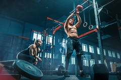 Het geschikte jonge mens het opheffen barbells uitwerken in een gymnastiek stock foto Het geschikte jonge mens het opheffen barbells uitwerken in een gymnastiek stock foto