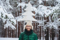 Het horizontale schot van het glimlachen mannelijk model houdt spar op hoofd, bevindt zich outdor in de winterbos, geniet van kal royalty-vrije stock foto Het horizontale schot van het glimlachen mannelijk model houdt spar op hoofd, bevindt zich outdor in de winterbos, geniet van kal royalty-vrije stock foto