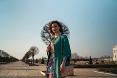Het jonge de vrouw van de manierminnaar waling in een park die levendig groen jasje en een kleurrijke rok dragen royalty-vrije stock afbeelding Het jonge de vrouw van de manierminnaar waling in een park die levendig groen jasje en een kleurrijke rok dragen royalty-vrije stock afbeelding