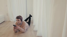 Het jonge meisje ligt op de vloer in haar handensmartphone stock videobeelden Het jonge meisje ligt op de vloer in haar handensmartphone stock videobeelden