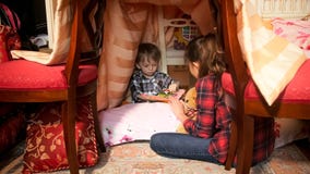 Het leuke boek van de de jongenslezing van de 1 éénjarigepeuter met oudere zuster in tent bij slaapkamer stock afbeeldingen Het leuke boek van de de jongenslezing van de 1 éénjarigepeuter met oudere zuster in tent bij slaapkamer stock afbeeldingen