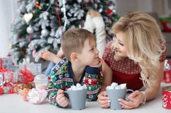 Het mamma en de zoon liggen dichtbij de Nieuwjaarboom met grote koppen cappuccino en heemst Stock Afbeelding Het mamma en de zoon liggen dichtbij de Nieuwjaarboom met grote koppen cappuccino en heemst Stock Afbeelding